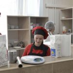 Two young adults in chef hats and aprons working side by side at a kitchen prep counter