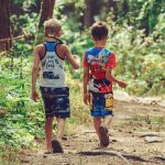 Two children walking together on a wooded camp trail