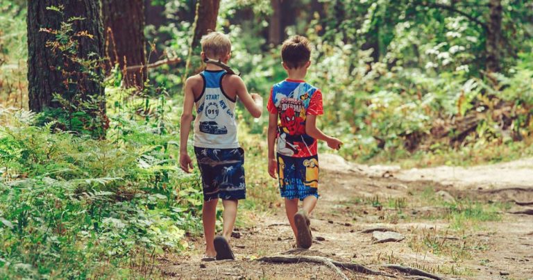 Two children walking together on a wooded camp trail