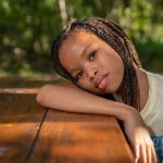 Girl resting at a camp picnic table outdoors with trees in the background