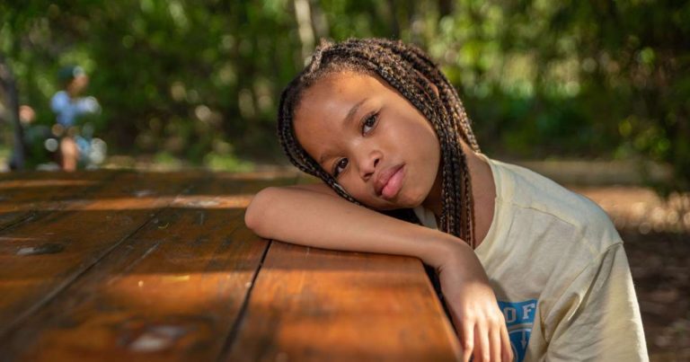Girl resting at a camp picnic table outdoors with trees in the background