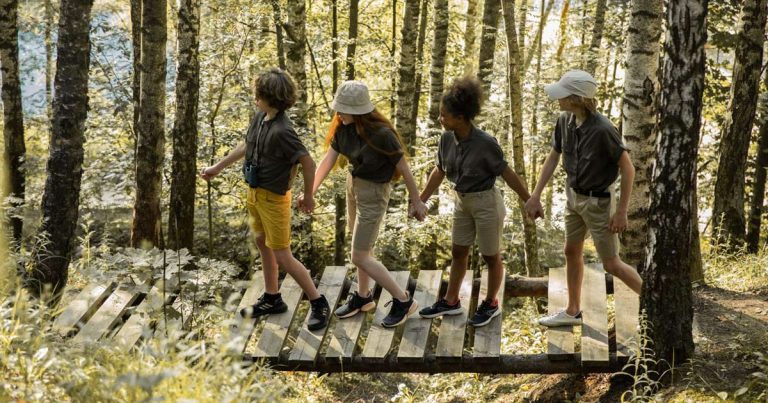 Four children crossing a wooden footbridge together through a birch forest at camp