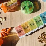 Prescription bottles and a labeled weekly pill organizer arranged on a wooden table in morning light