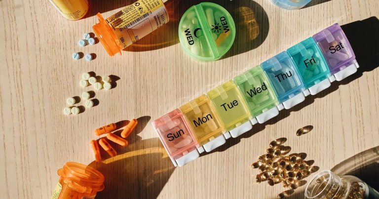 Prescription bottles and a labeled weekly pill organizer arranged on a wooden table in morning light