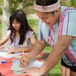 Camp staff member helping two young participants at an outdoor craft table