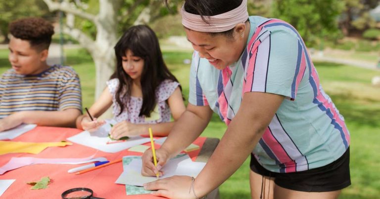 Camp staff member helping two young participants at an outdoor craft table