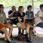 Camp staff members seated at picnic tables under an outdoor canopy during a staff session