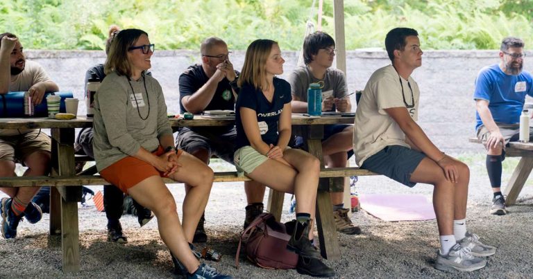 Camp staff members seated at picnic tables under an outdoor canopy during a staff session