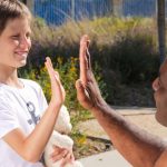 Staff member kneeling to give a high-five to a child with a stuffed animal outdoors