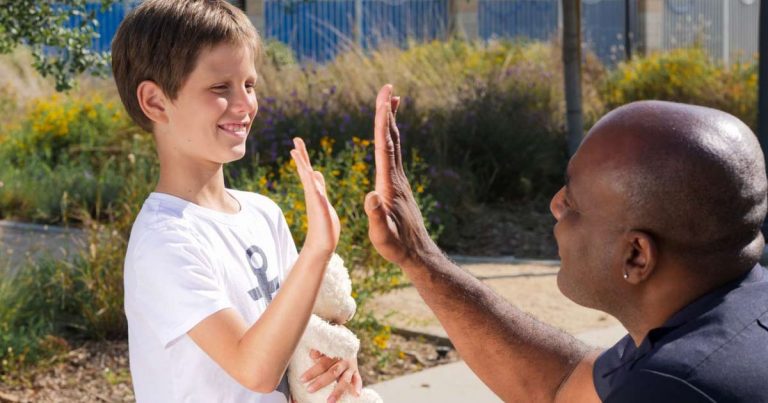 Staff member kneeling to give a high-five to a child with a stuffed animal outdoors