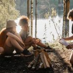 Group of teens gathered around a campfire by a lake at summer camp