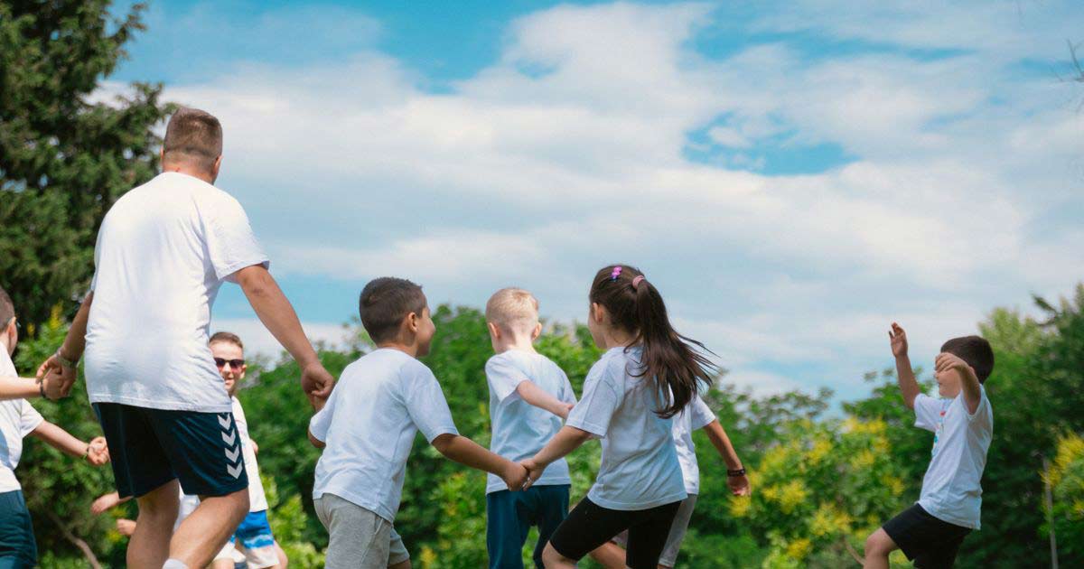Children holding hands and moving together in an outdoor group game under a bright sky